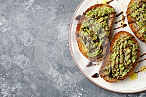 Flat lay of freshly made minced avocado toast with balsamico dressing, linseed or flaxseed and oil on a white plate, on