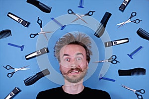 Flat lay funny face of bearded disheveled man and barber grooming hairdresser tools accessories on blue background. Barber shop,