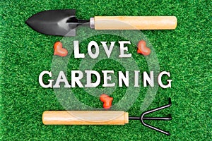 Flat-lay of garden hand tools and lettering LOVE GARDENING on grass