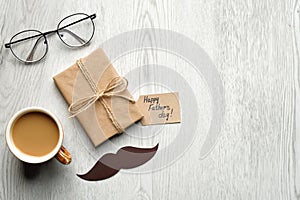 Flat lay gift box with label Happy Fathers Day, mustache, glasses, cup of coffee on wooden table. Top view Father`s day