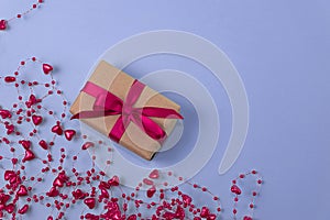 flat lay of gift with red bow next to beads with hearts on very peri color background. holiday concept