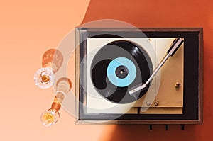 Flat lay gramophone record player from sixties. Turntable for single vinyl on orange background. Two cocktail glasses, party vibe