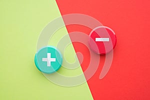 Flat lay of green plus and red minus symbol plastic button on green and red background with copy space. Concept of difference