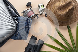 Flat lay grey suitcase with binoculars, hat, jeans, spinning for fishing and sandles on pastel background. travel concept - Image