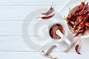 flat lay with grinded chili pepper in mortar with pestle on cutting board on white