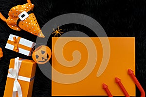 Flat lay of Halloween background with gift box decorative pumpkins, witch hat, postcard, red spear and spiders on black background