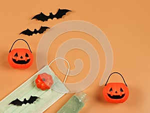 Flat lay of Halloween pumpkin , black paper bats,medical mask and alcohol sanitizer gel on orange background. Halloween , COVID-19