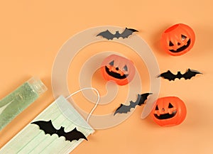 Flat lay of Halloween pumpkin , black paper bats,medical mask and alcohol sanitizer gel on orange background. Halloween , COVID-