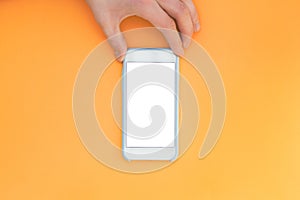 Flat lay hand with phone. The hand holds a smartphone with a white screen on top of a orange background.