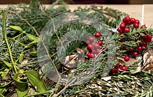 Flat lay of handcrafting supplies for red and green Christmas decorations with green fir branches and artificial red berries.