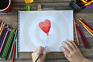 Flat lay of hands drawing a heart with colored pencils on white paper. Art studio workplace concept