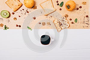 Flat lay healthy vegetarian breakfast composition. Cup of espresso coffee on white wooden table next to toast, fruits and nuts,