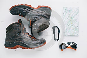 Flat lay of hiking boots, eyeglasses, carabiner and map