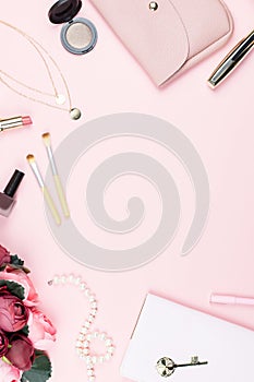 Flat lay home office desk. Female workspace with note pad, fashion accessories and make up products on pink background. Fashion or
