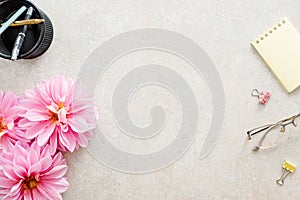 Flat lay home office desk. Female workspace with pink dahlia flowers, woman accessories, glasses on stone background. Top view
