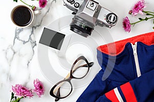 Flat lay home office desk. Female workspace with stylish clothes, glasses, vintage photo camera, coffee cup and flowers on marble