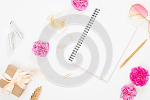 Flat lay home office desk. Top view blank paper notepad, pink rose flower buds, petals, female accessories, gift box on white