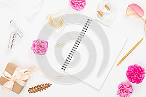 Flat lay home office desk. Top view blank paper notepad, pink rose flower buds, petals, female accessories, gift box on white