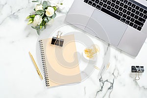 Flat lay home office desk. Women workspace with laptop computer, diary, flowers bouquet, golden accessories on white marble