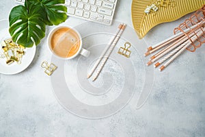 Flat lay home office feminine table with coffee cup, golden accessories, computer keyboard and tropical leaves on grey background