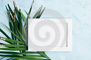 Flat lay horizontal photo frame mock up with green and gold palm leaves on blue background. Travel concept