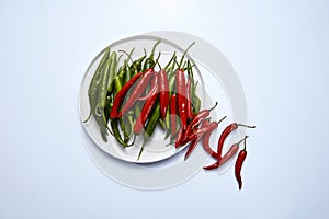 Flat lay of hot chili pepper green and red in a white plate on a white background.