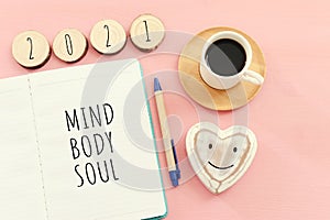 Flat lay image of notebook with words Mind, Body, Soul on pink wooden background