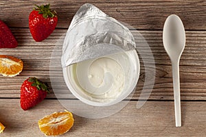 A white plastic cup of plain greek yogurt with a peeled off aluminum foil seal and a disposable plastic spoon