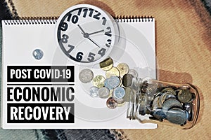 POST COVID-19 ECONOMIC RECOVERY text on the book with clock and coins spilling out of from jar. photo