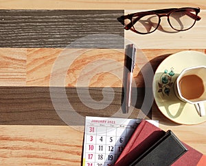 Flat lay of january calendar 2021 with tea cup, glasses, pen, diary on wooden background