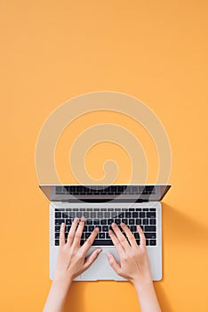 Flat lay of laptop, coffee and notebook on yellow background. Female hands typing on keyboard