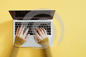 Flat lay of laptop, coffee and notebook on yellow background. Female hands typing on keyboard