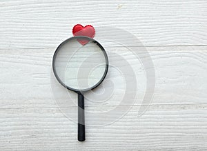 flat lay a magnifying glass and decorative red hearts isolated on a white wooden background