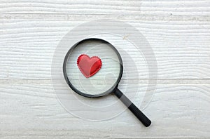 flat lay a magnifying glass and decorative red hearts isolated on a white wooden background