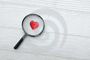 flat lay a magnifying glass and decorative red hearts isolated on a white wooden background