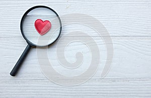 flat lay a magnifying glass and decorative red hearts isolated on a white wooden background