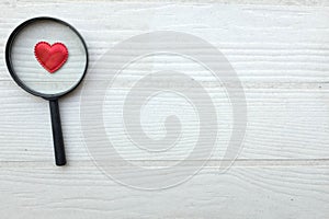 flat lay a magnifying glass and decorative red hearts isolated on a white wooden background