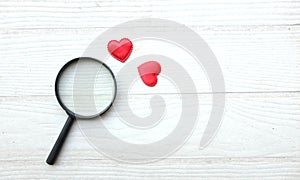 flat lay a magnifying glass and decorative red hearts isolated on a white wooden background