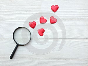 flat lay a magnifying glass and decorative red hearts isolated on a white wooden background