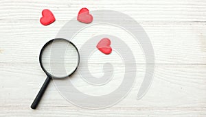 flat lay a magnifying glass and decorative red hearts isolated on a white wooden background