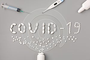 Flat lay of medicine pills shape as word covid 19 with syringe, thermometer and pills on gray background