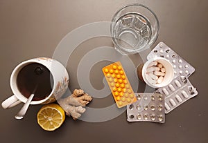 Flat lay: medicines, glass of water and natural tea with ginger and lemon for immunity boosting