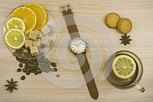 Flat lay. Men`s watches with leather strap. Cup of tea with lemon. Slices of lemon and orange on a saucer. Coffee beans, cookies