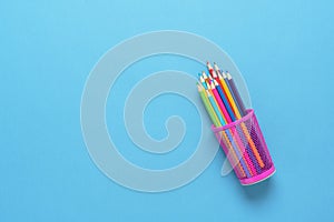 Flat lay metal glass with colored pencils on blue paper background. Stationery, top view