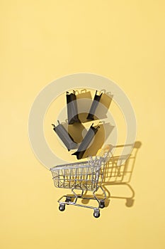 Flat lay miniature supermarket cart with shopping bags in black friday sale on yellow background