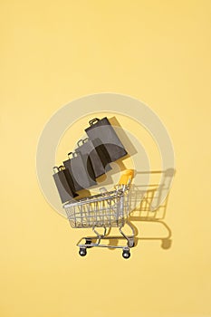 Flat lay miniature supermarket cart with shopping bags in black friday sale on yellow background