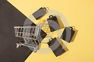 Flat lay miniature supermarket cart with shopping bags in black friday sale on yellow background