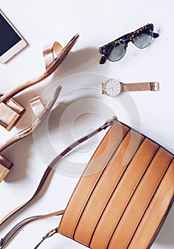 Flat lay of a minimal set of female accessories:golden wrist watch, mid heel sandals with ankle strap, leather buckle bag, mobile