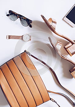 Flat lay of a minimal set of female accessories:golden wrist watch, mid heel sandals with ankle strap, leather buckle bag, mobile