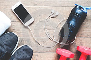 Flat lay of mobile phone with earphones and sport equipments on wood background. Workout and fitness